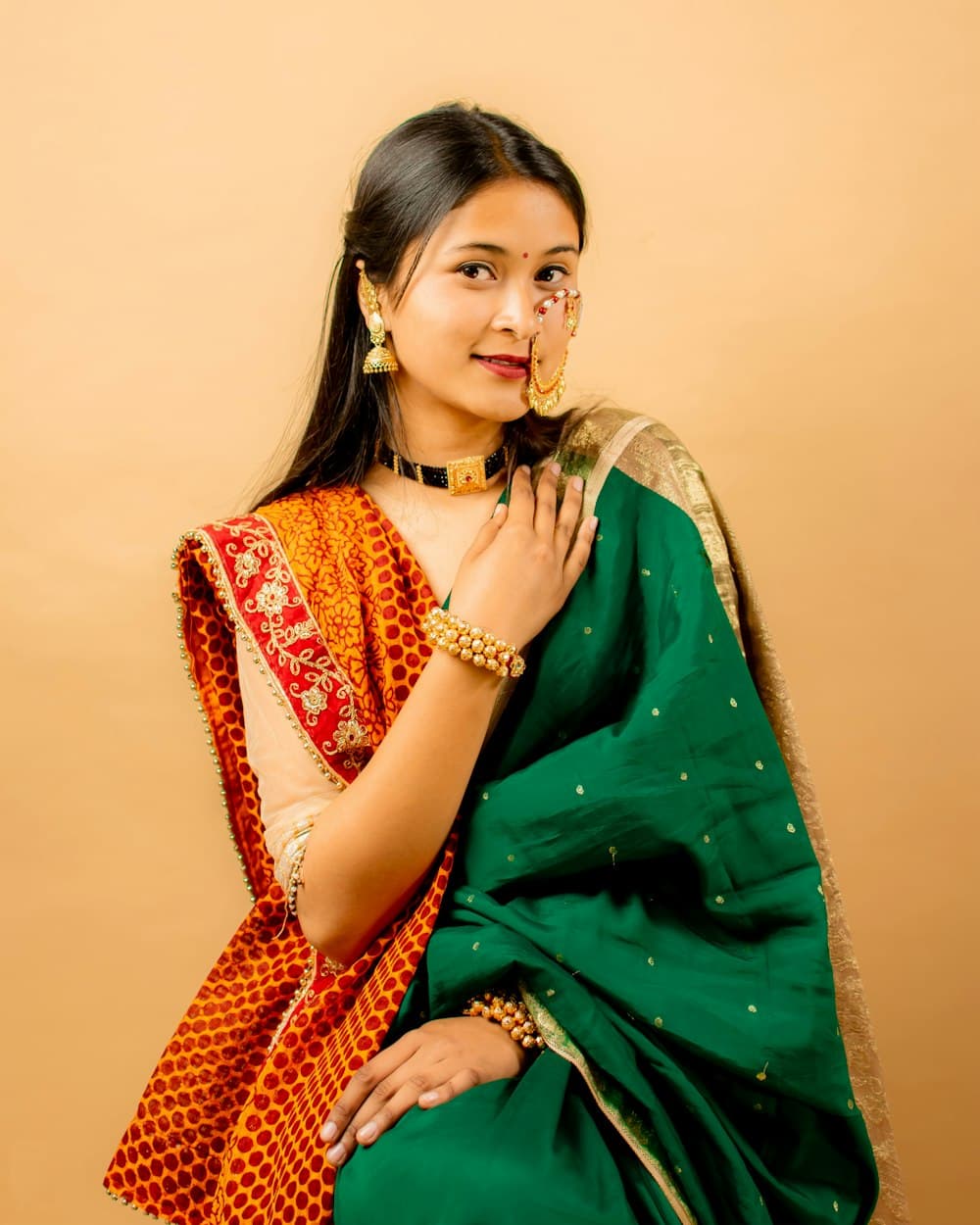 A woman in a green saree with an orange and gold pallu draped over her shoulder
