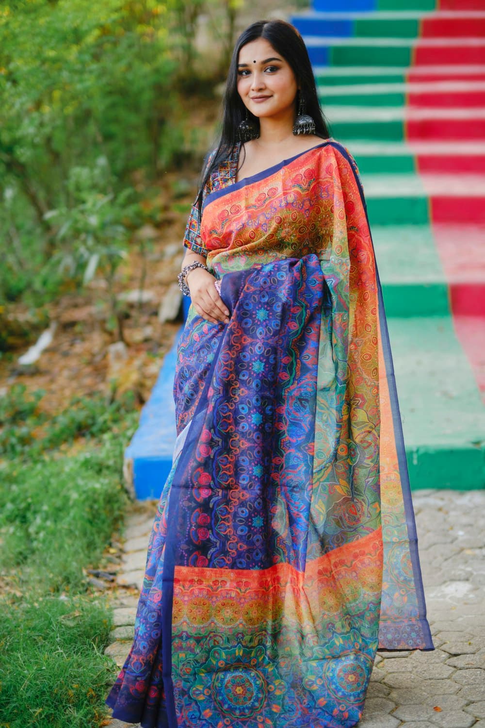 A woman in a blue saree with a multicoloured printed pallu on garden steps