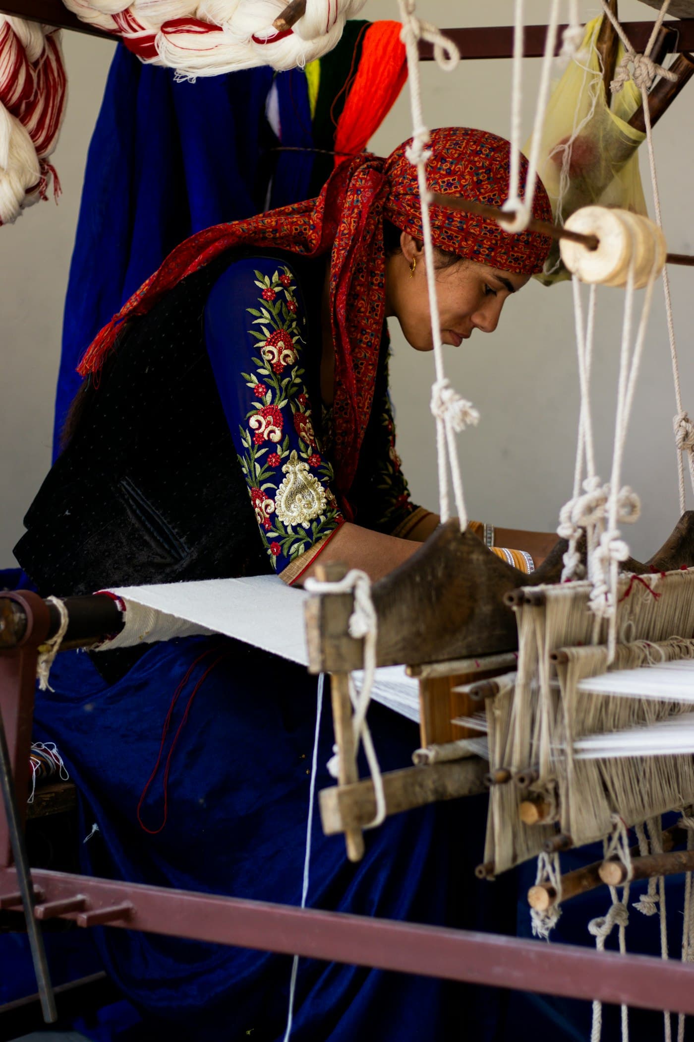 A weaver works at a wooden handloom, threads stretched in front of her